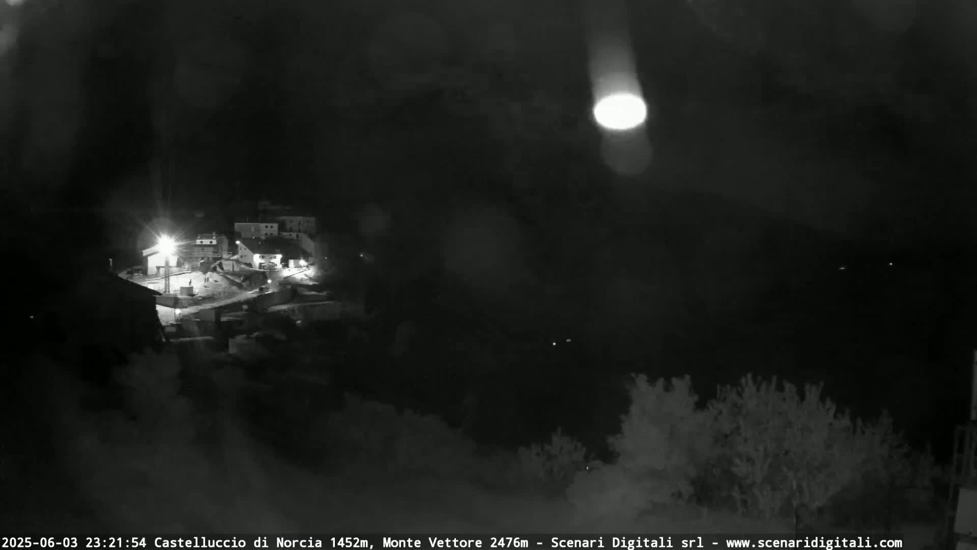 A nighttime, low-light view of a small village nestled in a dark landscape.