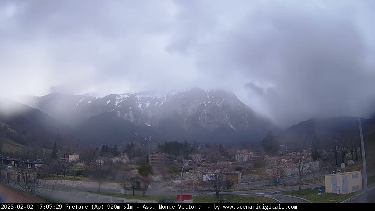 A snow-capped mountain range is visible through a misty, overcast sky, behind a small town nestled in a valley.