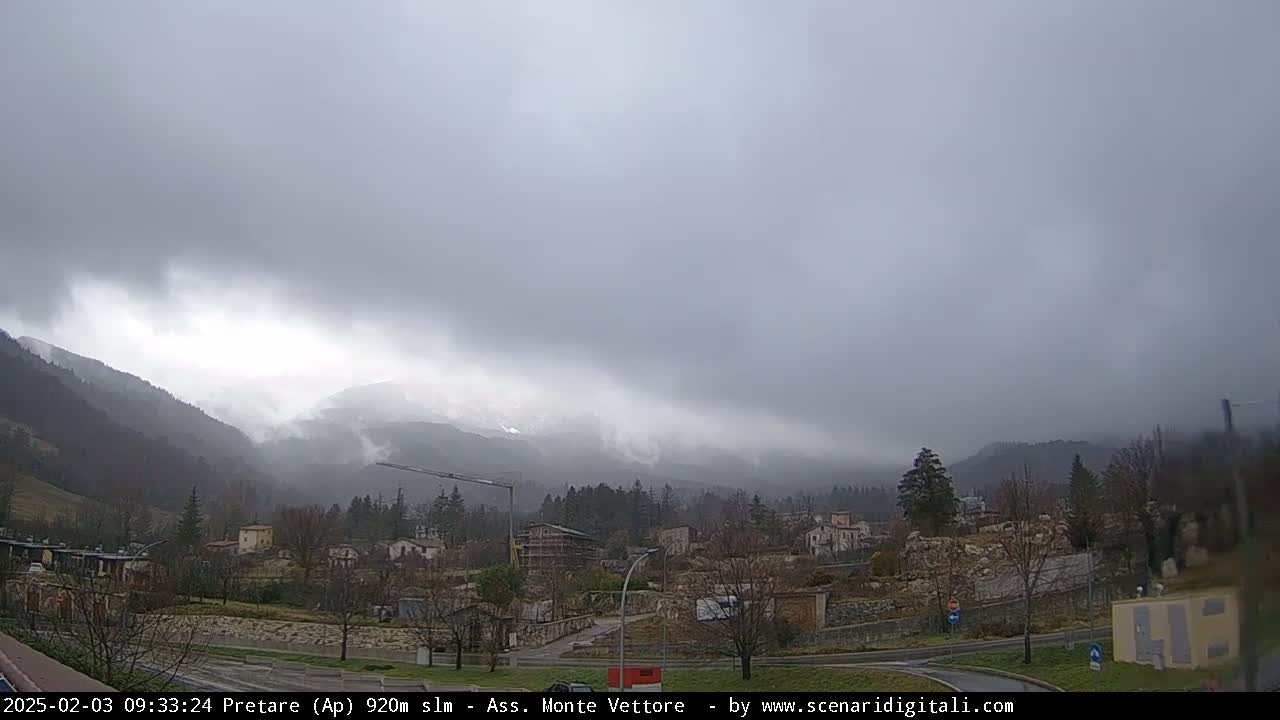 A small town nestled in a valley between misty mountains under an overcast sky.
