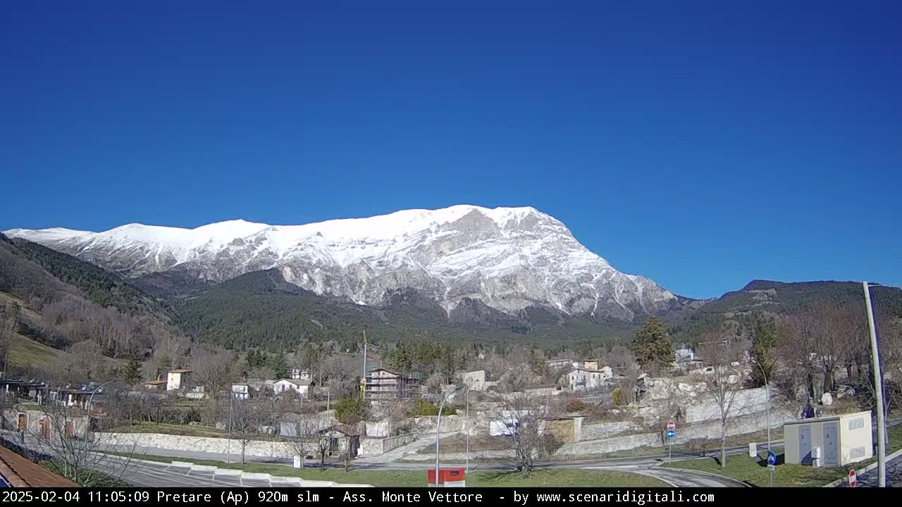 A snow-capped mountain looms over a small town under a clear blue sky.