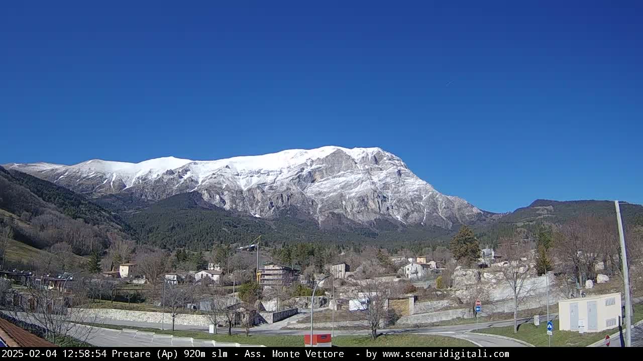 A snow-capped mountain looms over a small town under a clear blue sky.