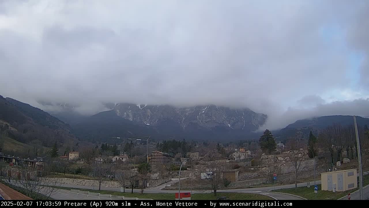 A small town nestled in a valley, with snow-capped mountains shrouded in fog in the background.