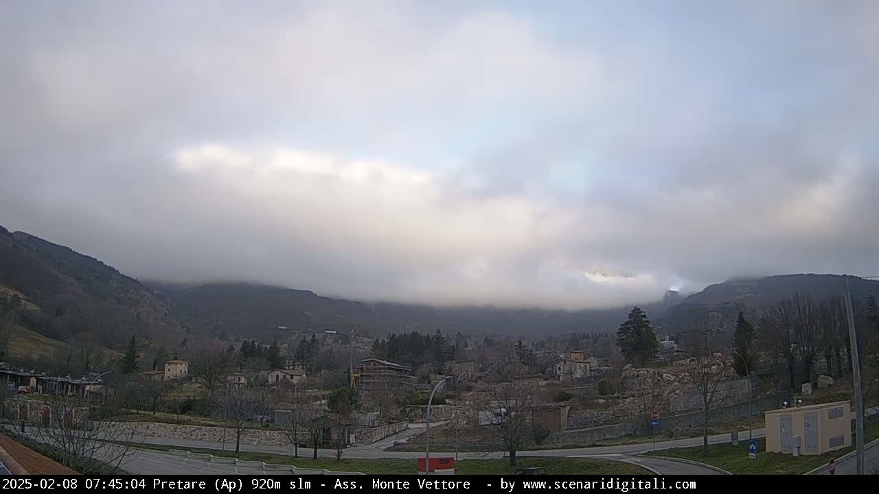 A foggy, overcast day reveals a valley town nestled between low, tree-covered mountains.