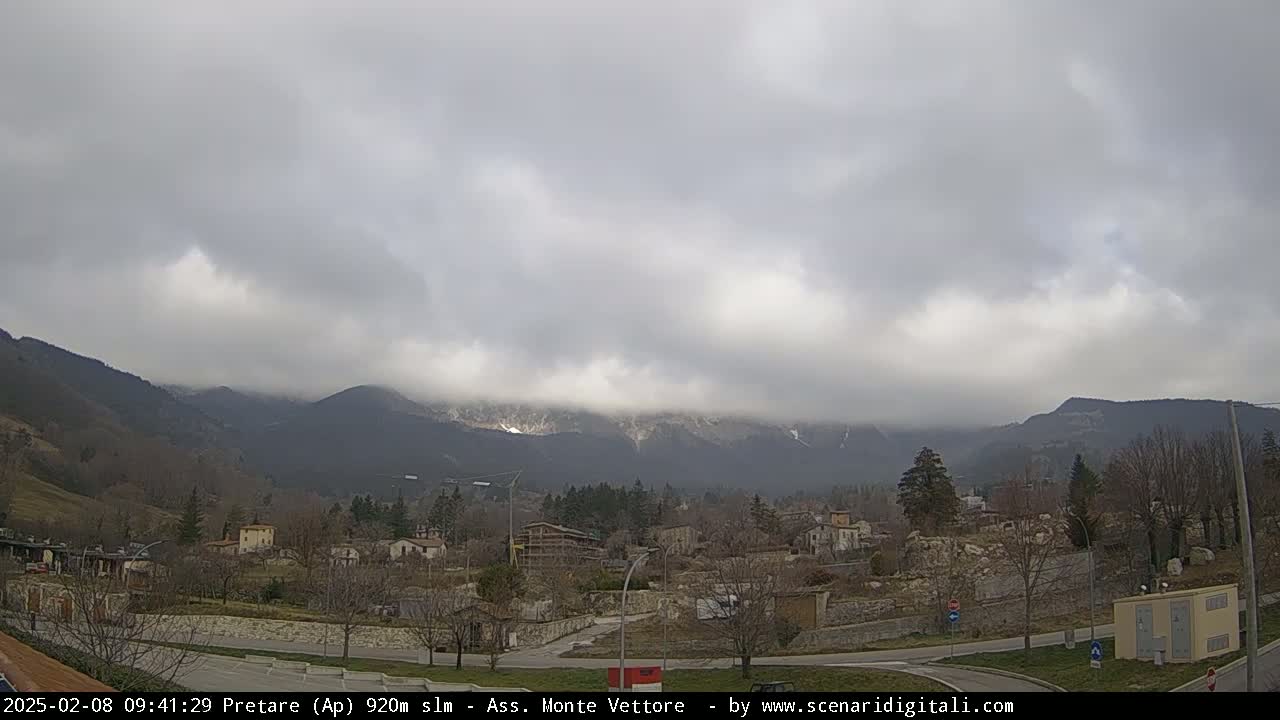 A small town sits in a valley, overlooked by overcast mountains with hints of snow.