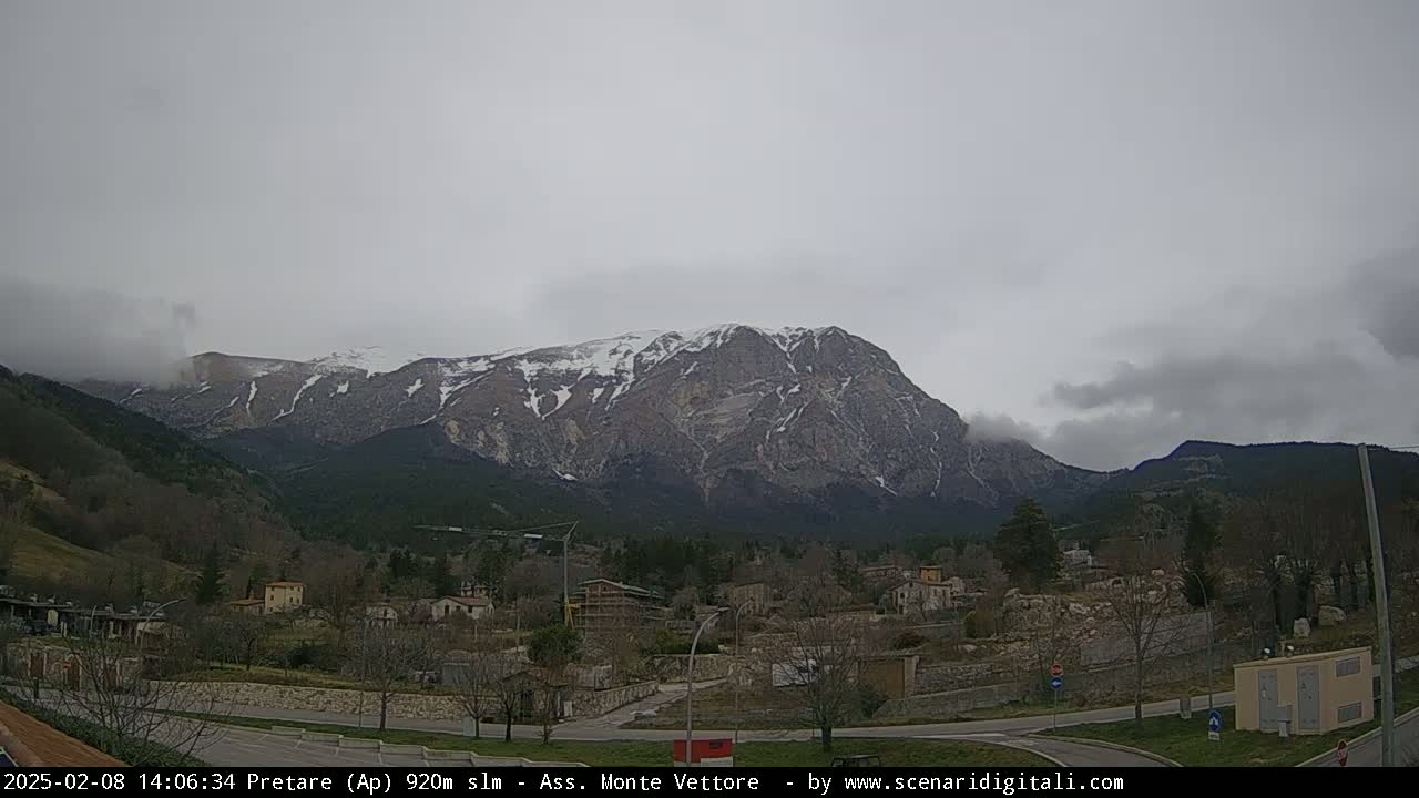 A snow-capped mountain range looms over a small town under an overcast sky.