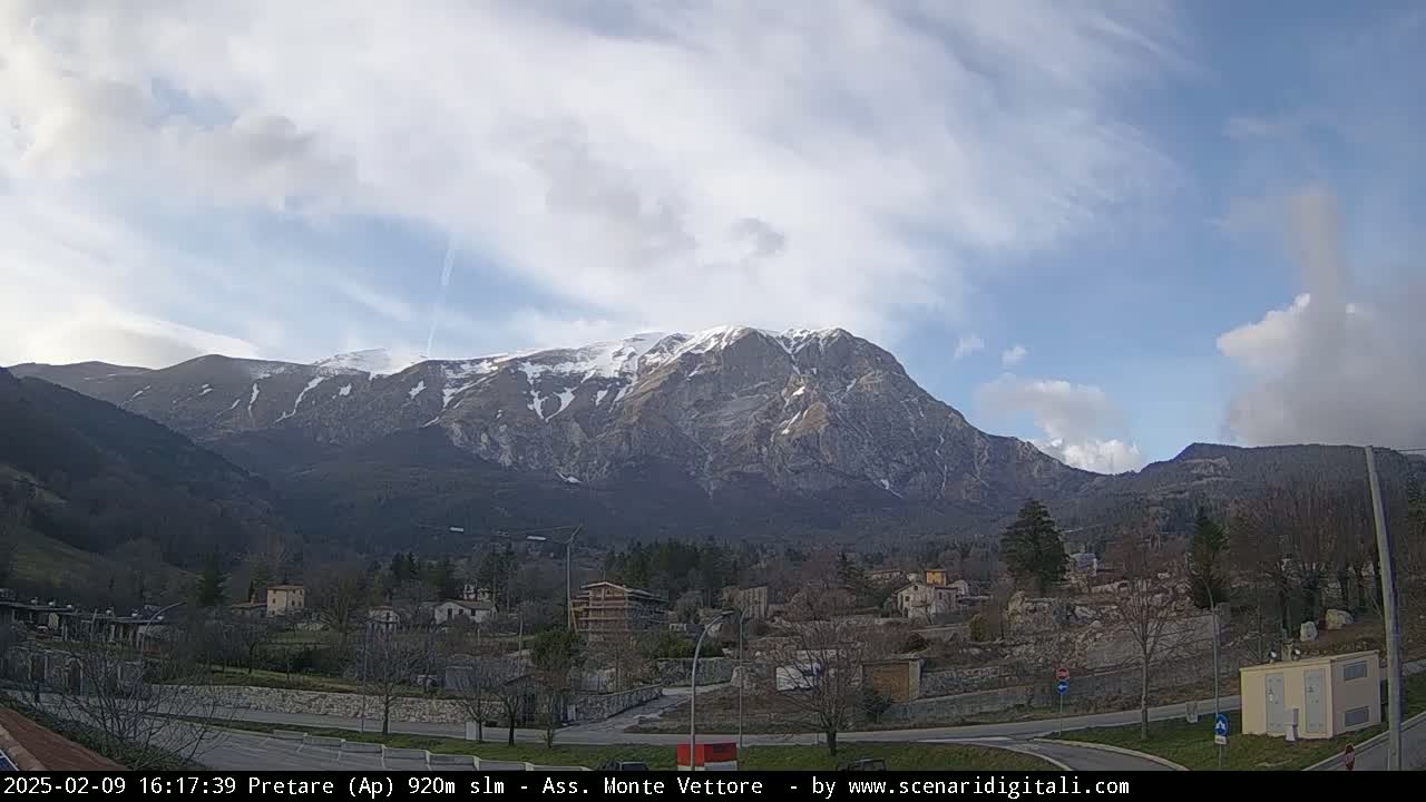 A partially snow-capped mountain range is visible in the background, overlooking a small town under a partly cloudy sky.