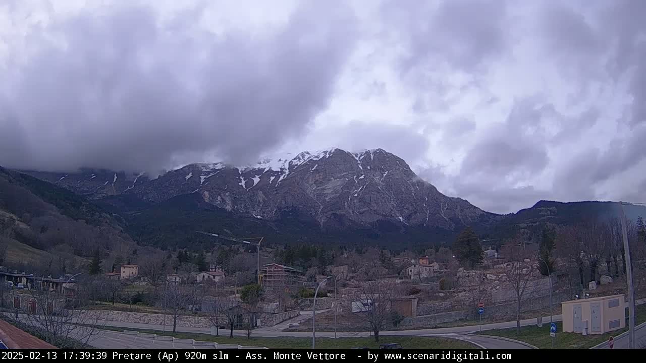 A snow-capped mountain range looms over a small town under a cloudy sky.