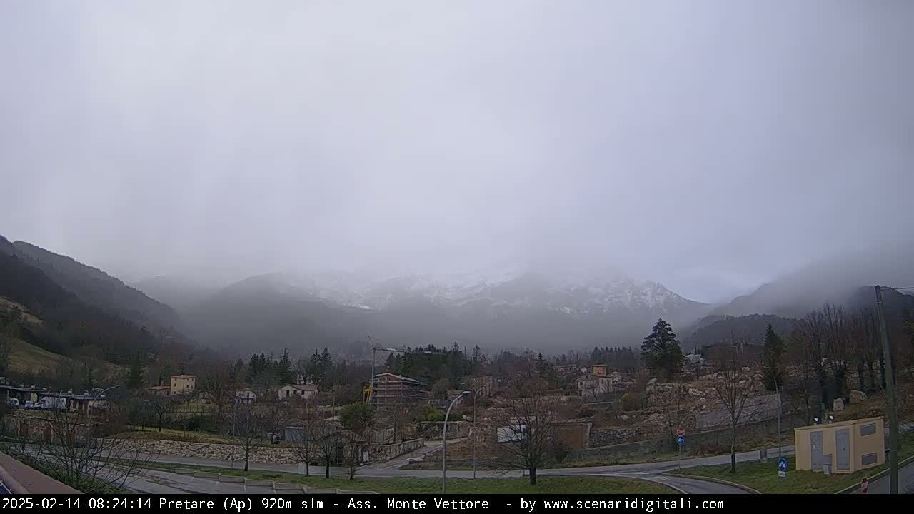 A foggy, overcast day reveals a snow-dusted mountain range behind a small town nestled in a valley.