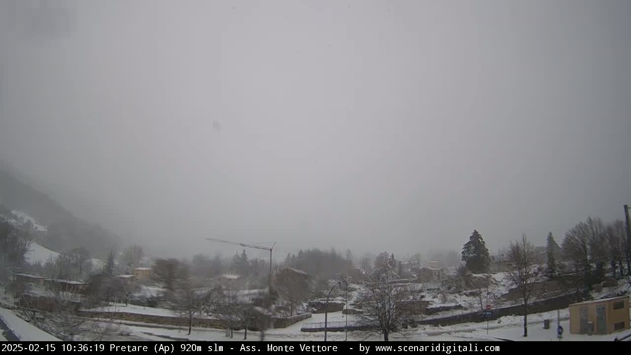 A snow-covered village is visible under a heavy, gray sky, with light snowfall.
