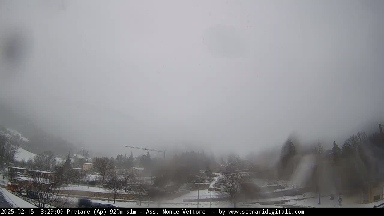 A snow-covered town is partially obscured by heavy fog or mist under an overcast sky.