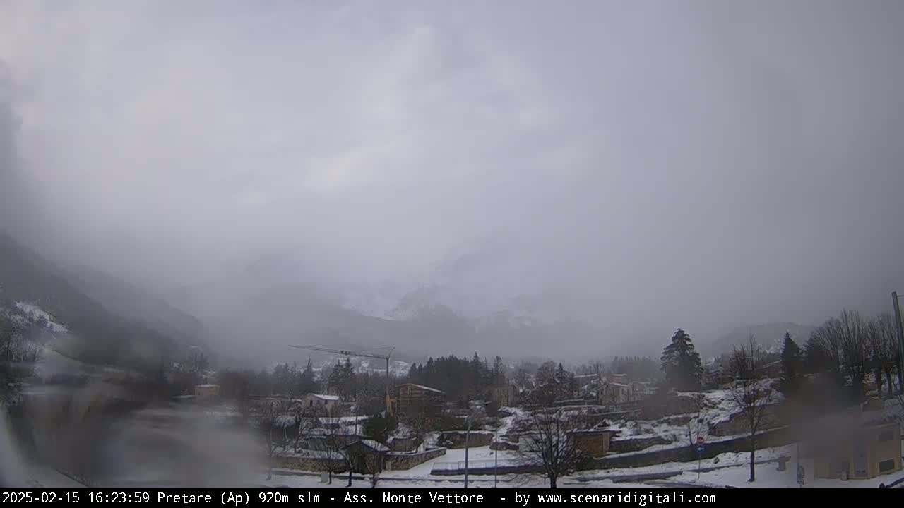 A foggy, snowy landscape shows a small town nestled in a valley between mountains.