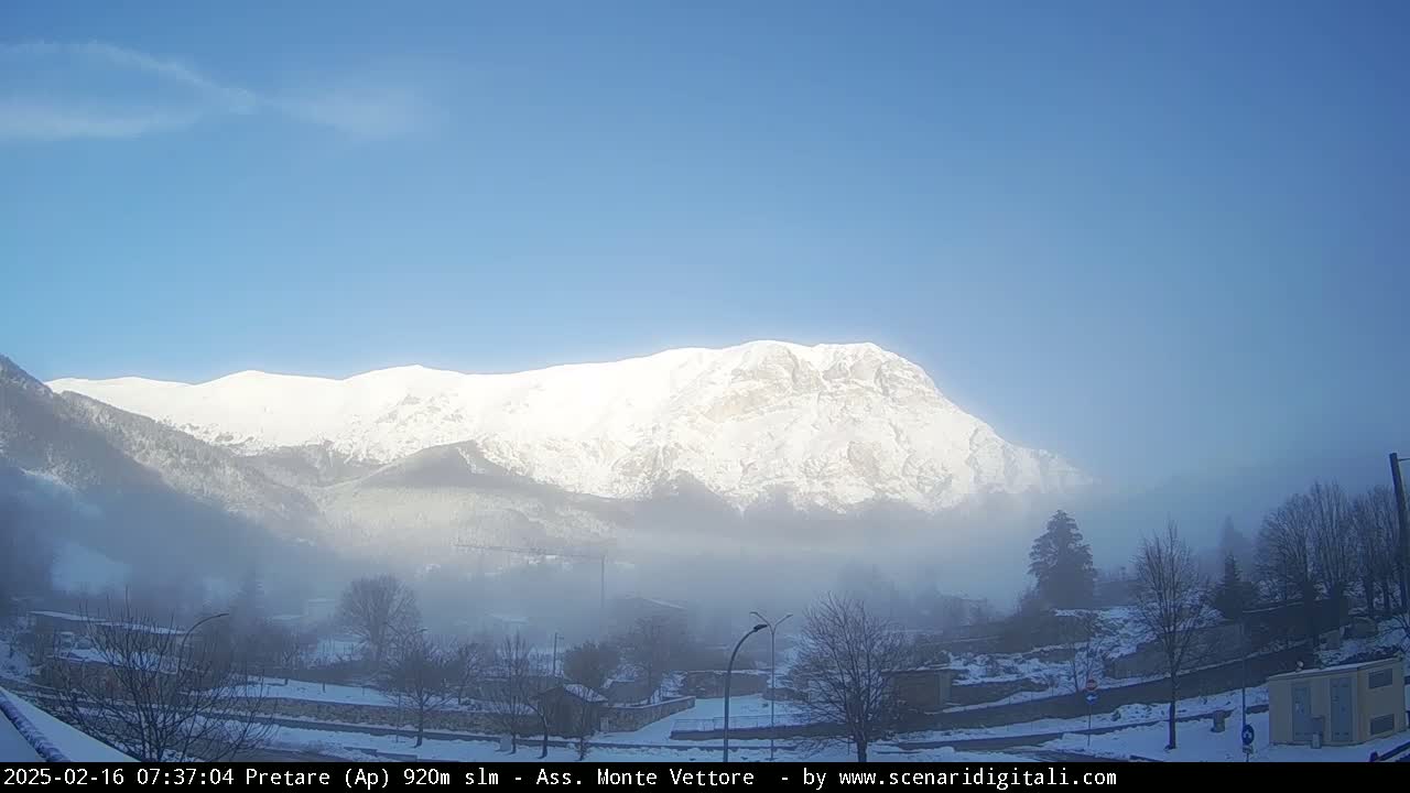 A snow-covered mountain range is visible in the distance under a clear blue sky, with a foggy valley in the foreground.