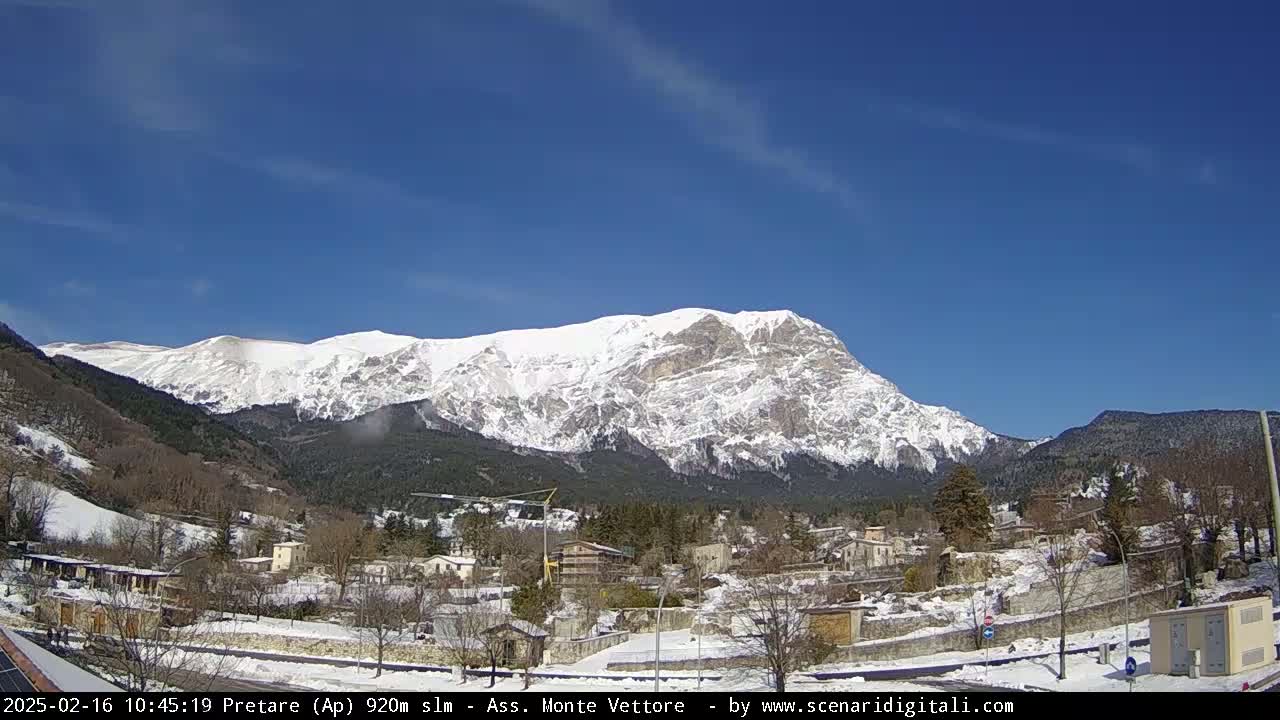 A snow-covered mountain looms over a small village under a clear blue sky.