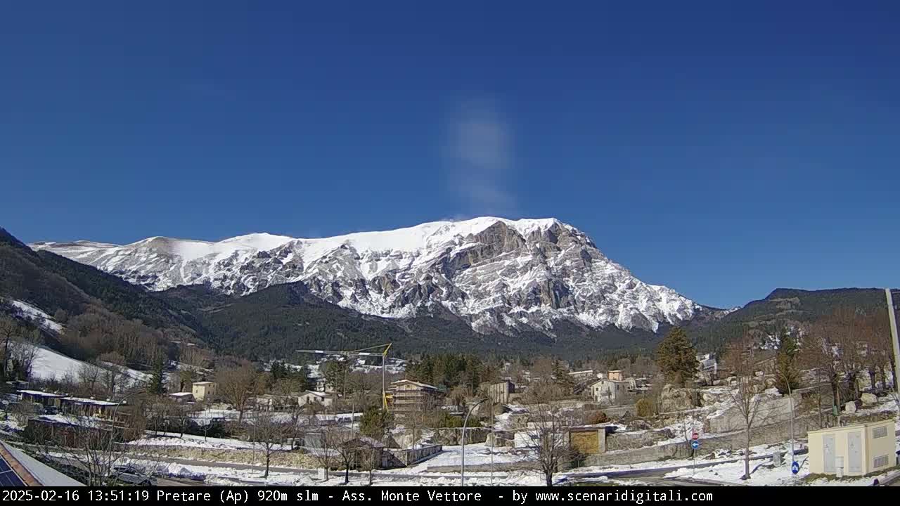 A snow-covered mountain rises above a small village under a clear blue sky.