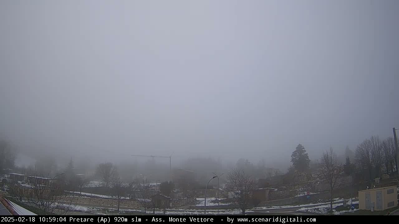 A foggy, snowy landscape shows a town nestled among bare, winter trees and a construction crane.