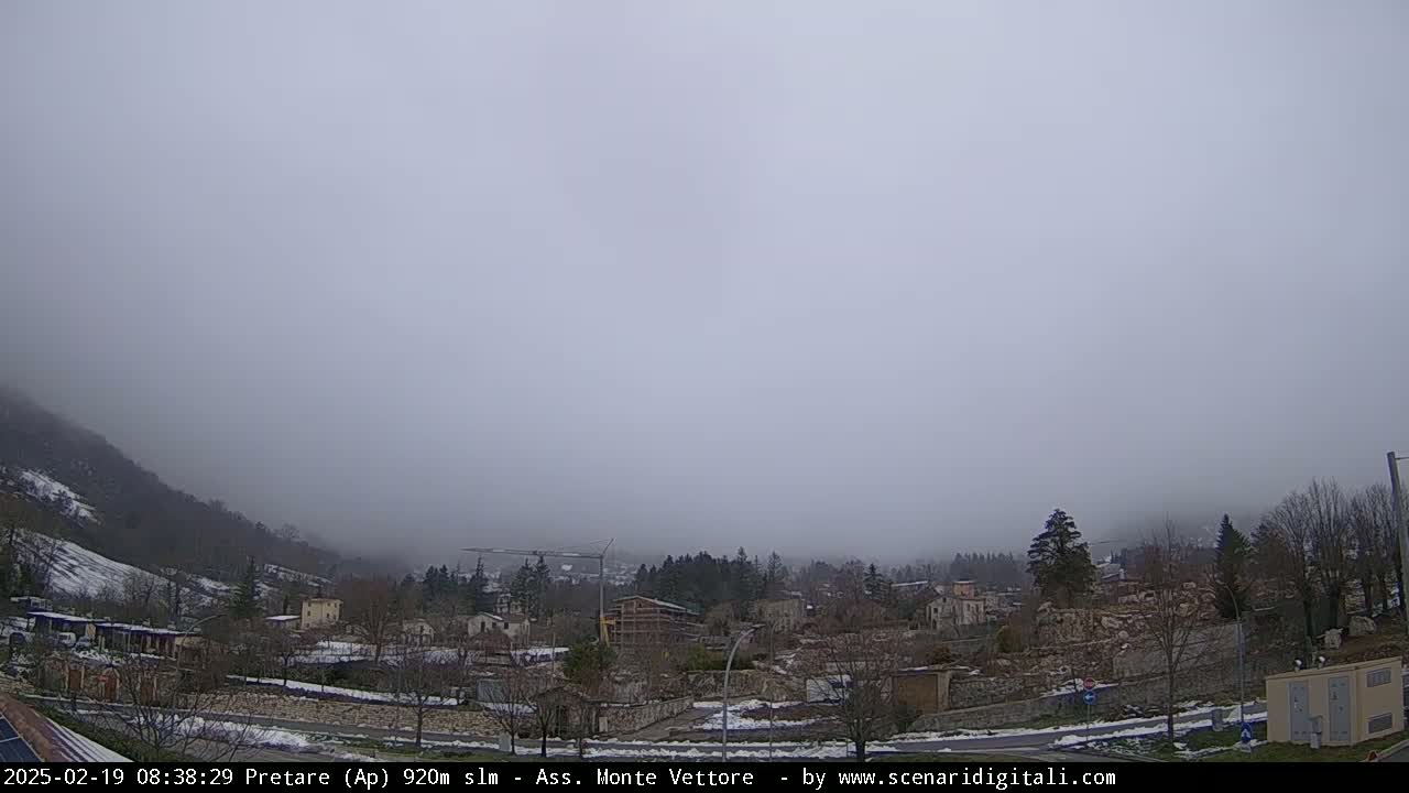 A foggy, snowy landscape shows a small town nestled in a valley between low mountains.