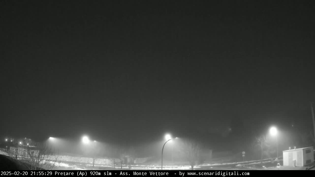 A foggy night scene shows a roadway lit by several streetlights.
