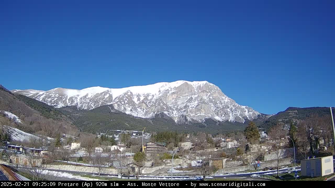 A snow-capped mountain looms over a small town under a clear blue sky.