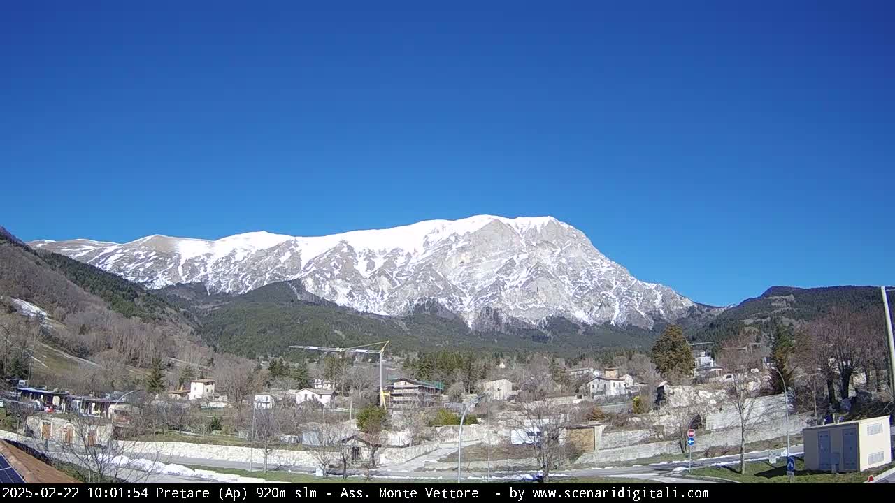 A snow-capped mountain looms over a small village under a clear blue sky.