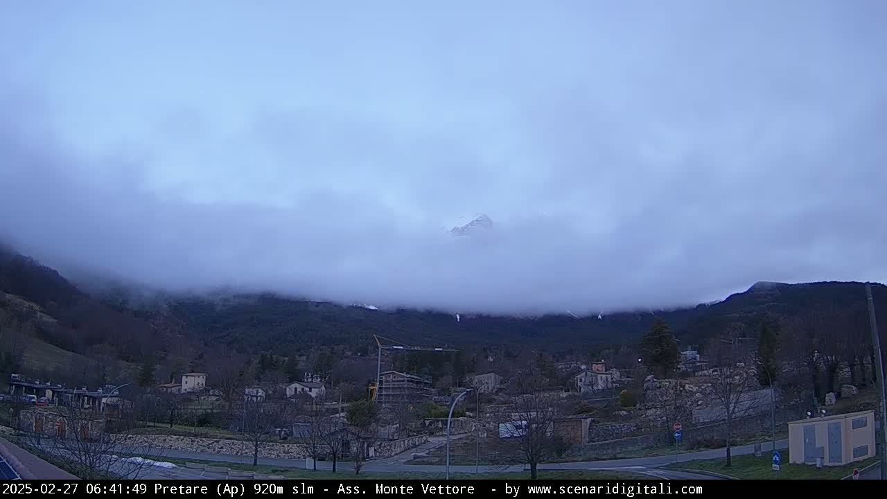 A foggy, overcast day reveals a small village nestled at the base of a mountain partially obscured by low-lying clouds.