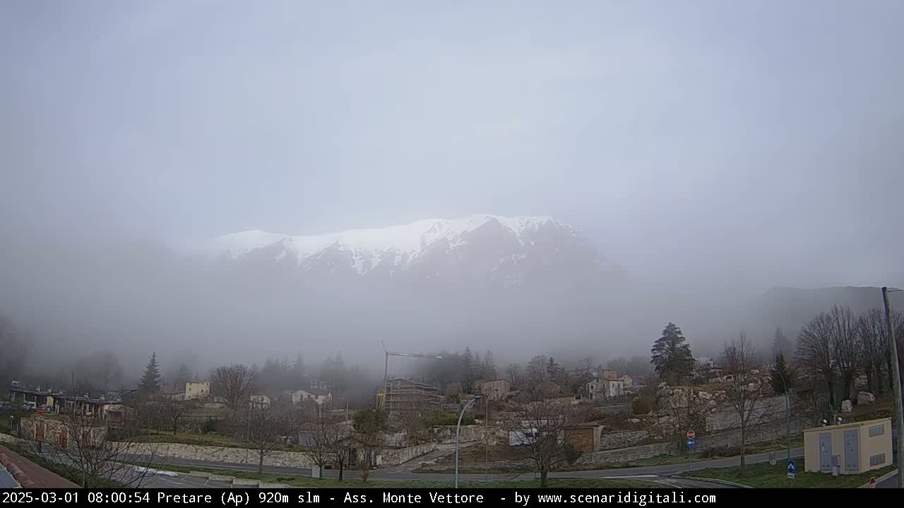 A snow-capped mountain range is visible through a thick fog, overlooking a small town.