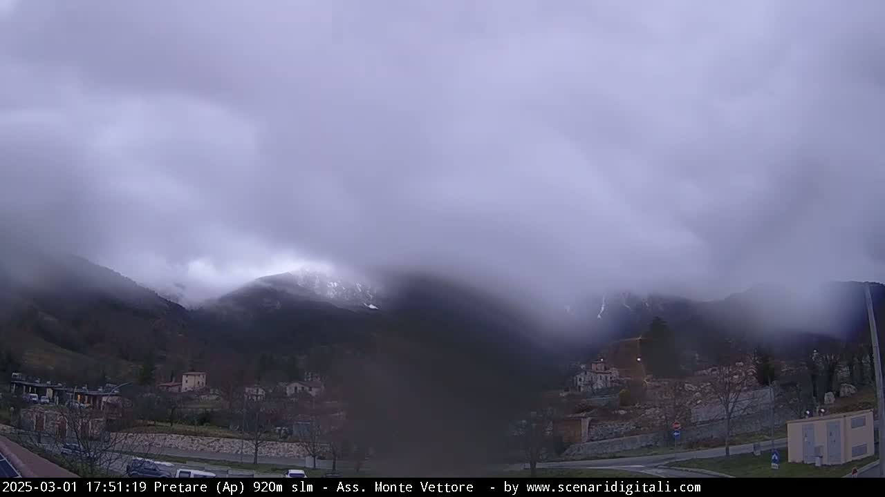 A misty, overcast day reveals a snow-dusted mountain range behind a small town nestled in a valley.