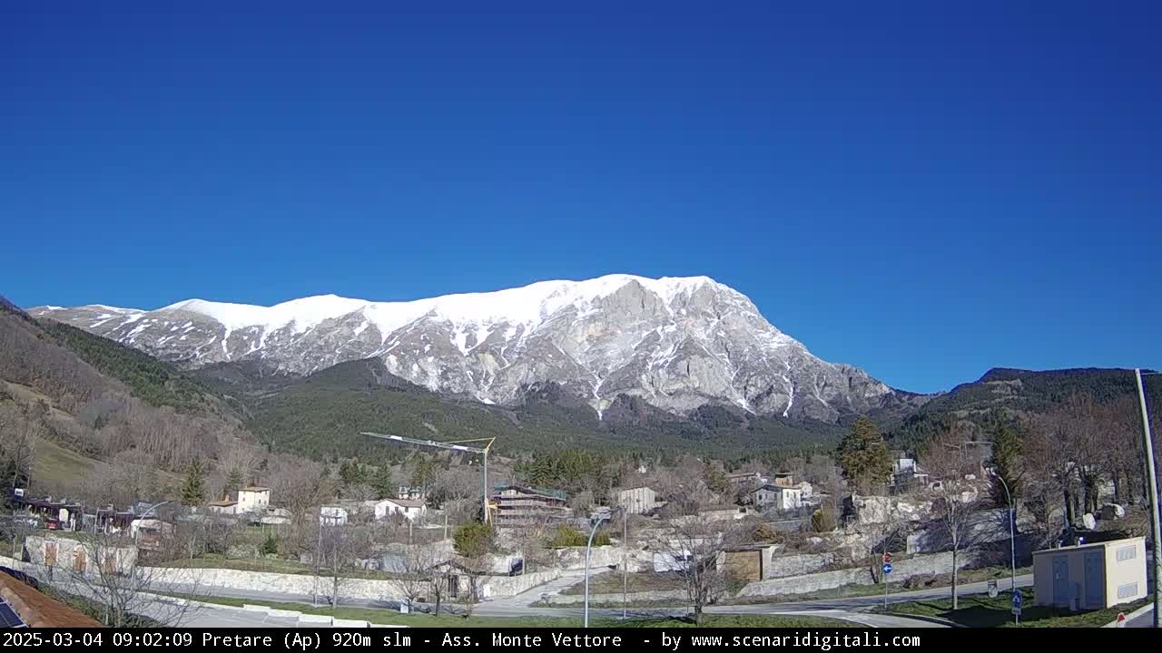 A snow-capped mountain rises behind a small village on a clear, sunny day.