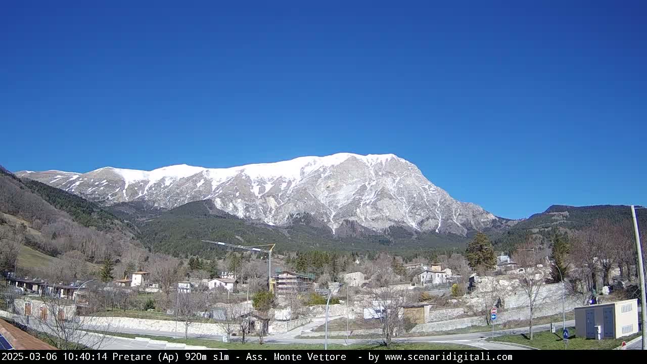 A snow-capped mountain rises in the background of a small village under a clear blue sky.