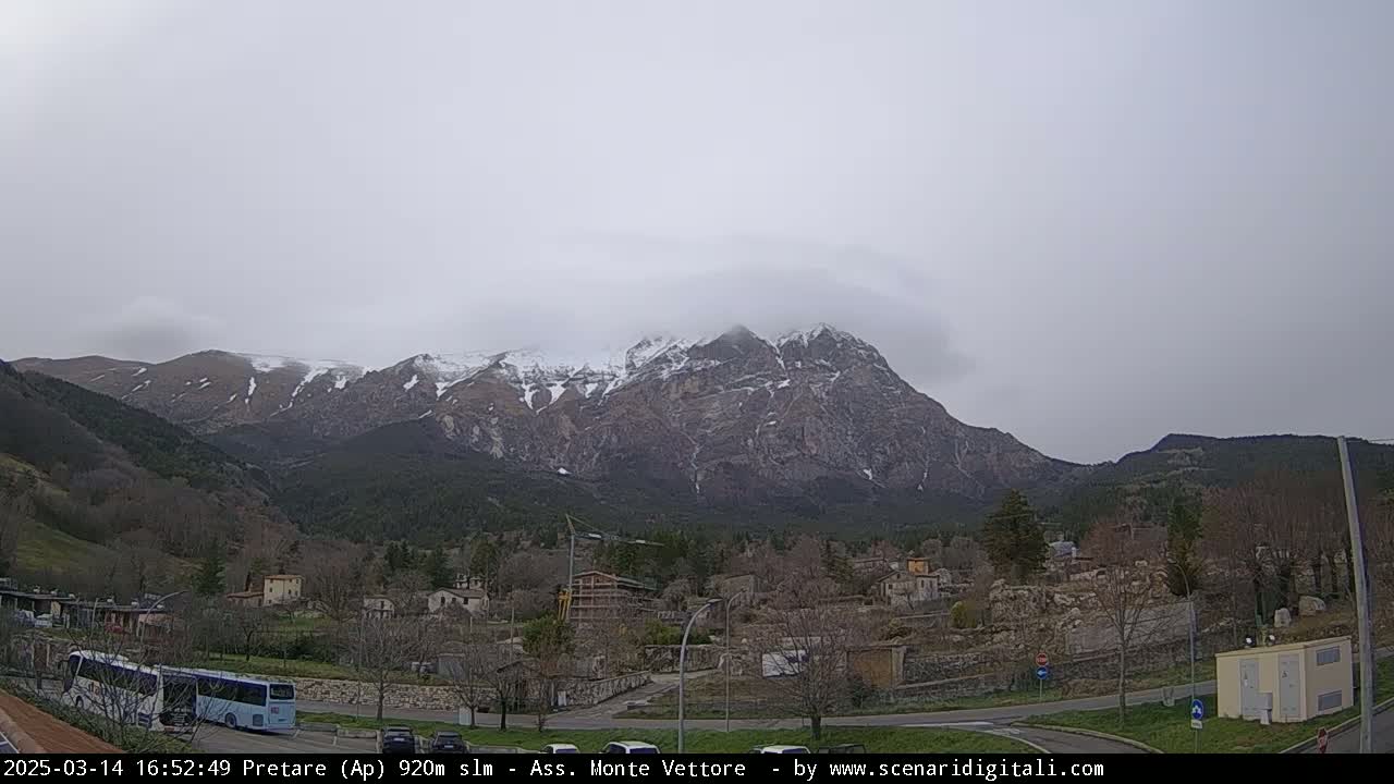 A snow-capped mountain range looms over a small village under an overcast sky.