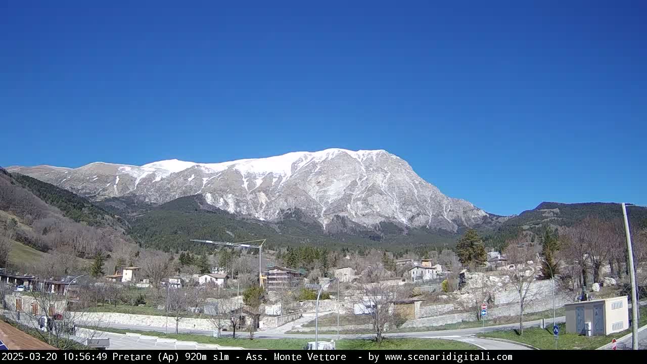 A snow-capped mountain looms over a small village under a clear blue sky.