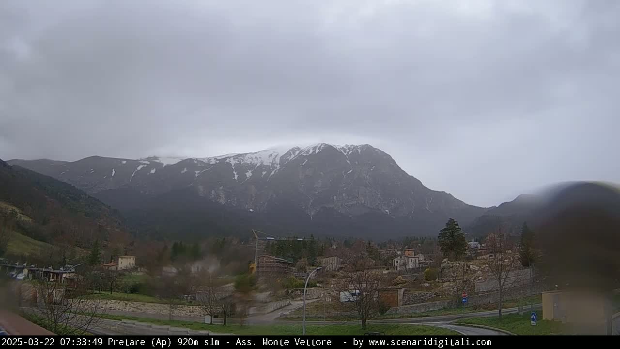A snow-dusted mountain range looms over a small town on an overcast day.