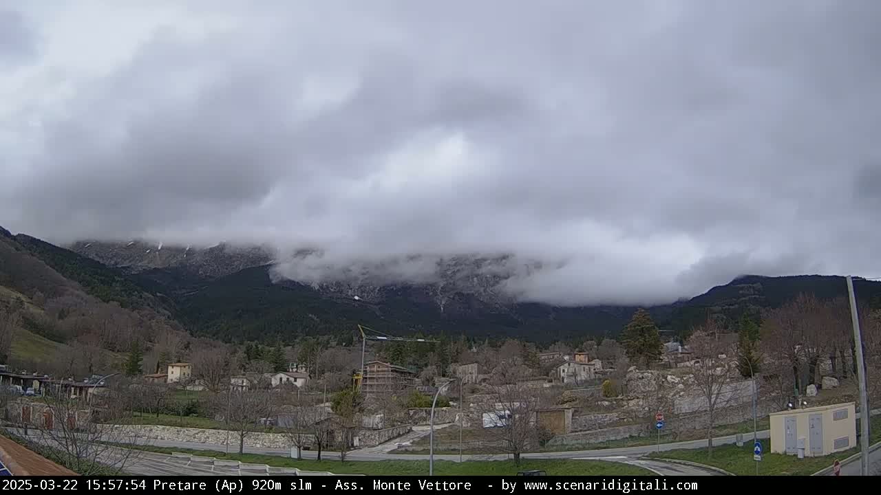 A cloudy day reveals a small village nestled at the foot of snow-dusted mountains.