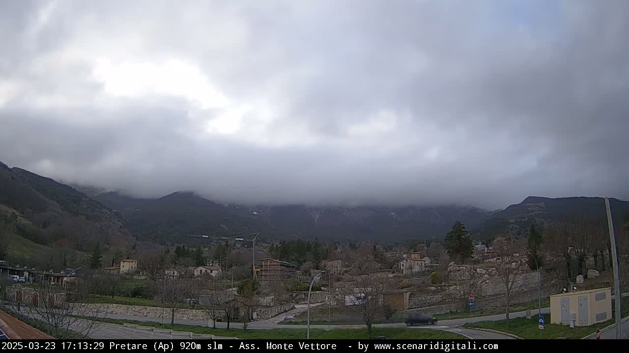 A small town nestled in a valley, surrounded by overcast mountains partially shrouded in fog.