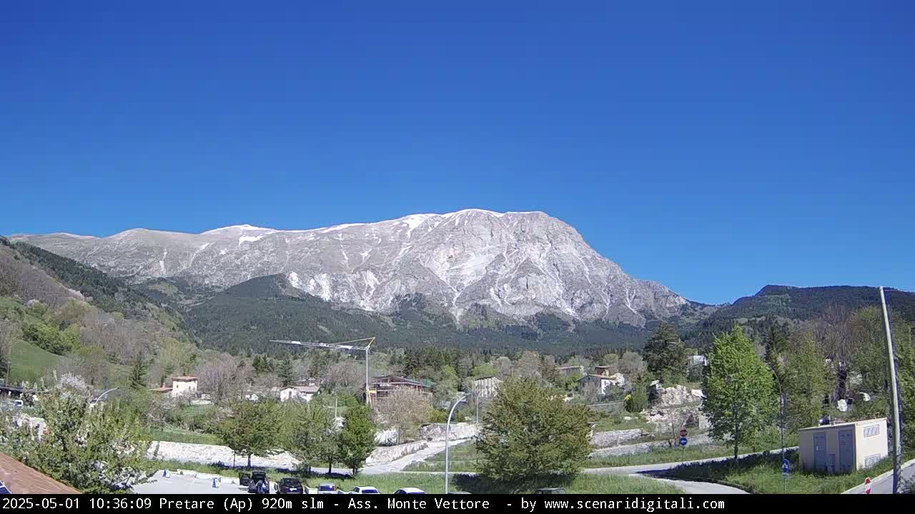 A snow-capped mountain looms over a small town nestled in a valley under a clear blue sky.