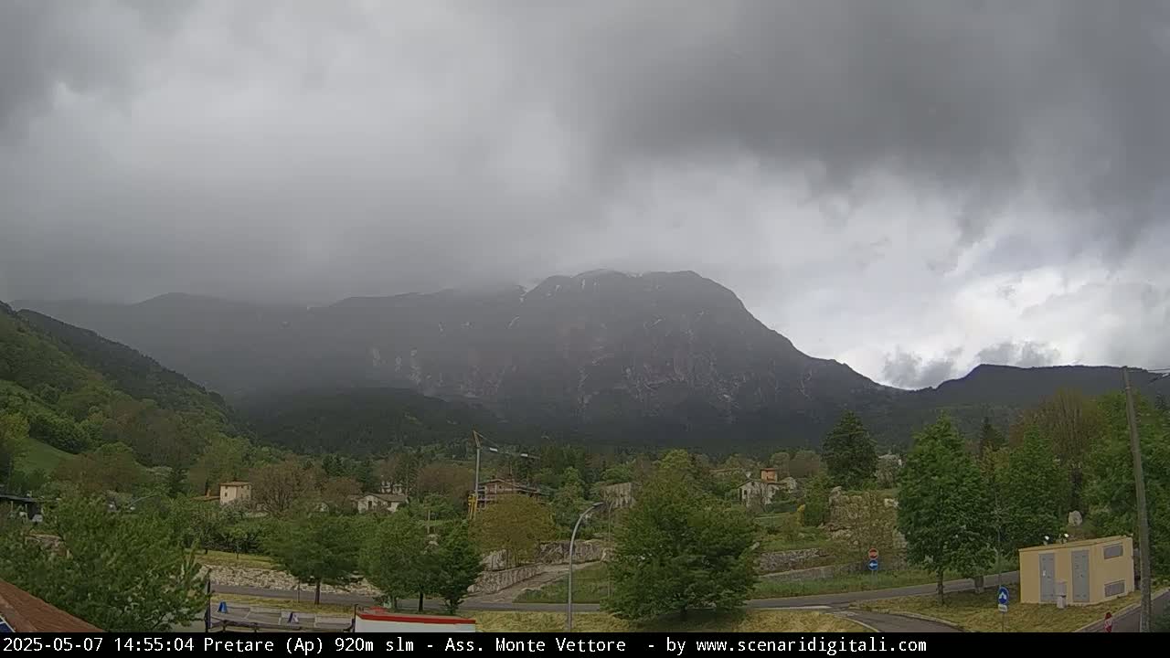 A hazy, overcast day reveals a mountain range behind a small village nestled in a valley of green trees.