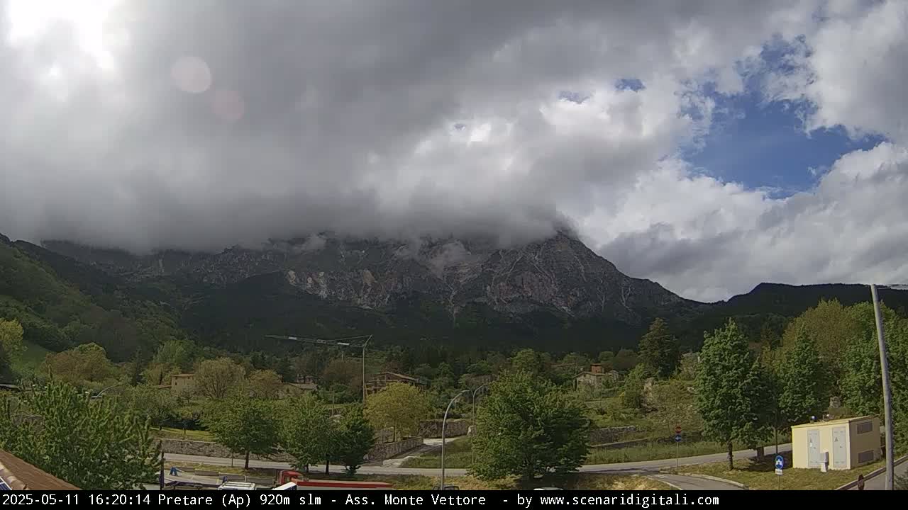 A partly cloudy sky hangs over a valley of green trees and buildings, with a large mountain shrouded in mist in the background.
