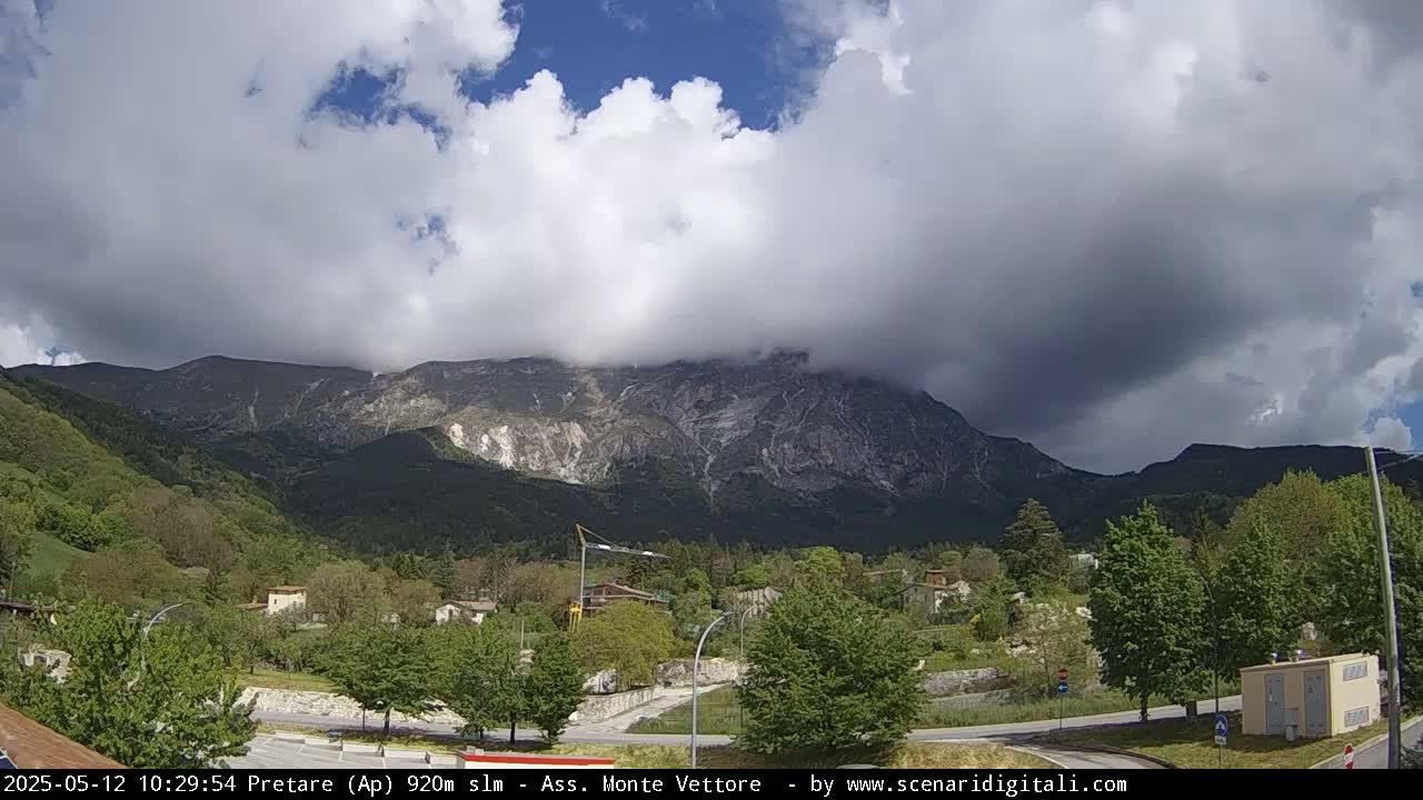 A partly cloudy sky hangs over a mountain range and a small town nestled in a valley.