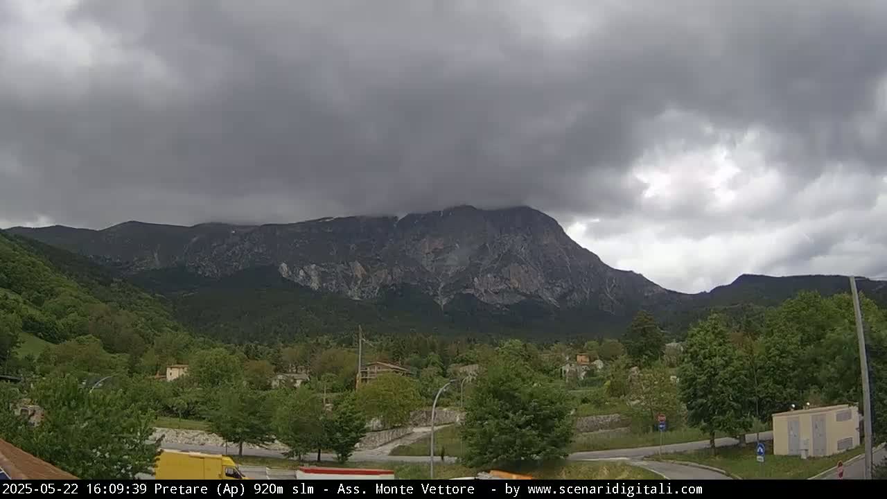 A large, rocky mountain is visible in the distance under a cloudy, overcast sky, with green vegetation and a small town in the foreground.