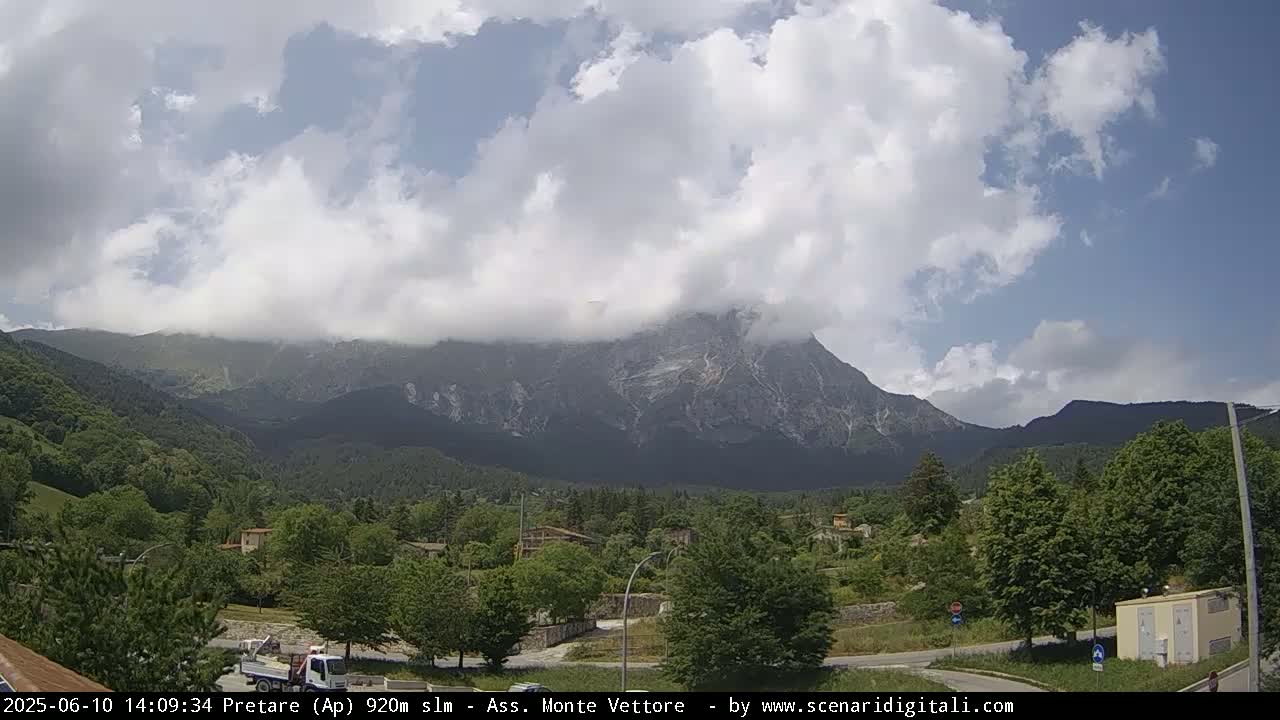 A partly cloudy day reveals a mountain range, with a village nestled in the valley below.