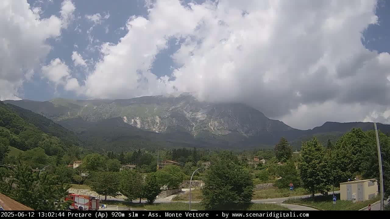 A partly cloudy day reveals a mountain range in the distance, with lush green vegetation and a small town nestled in the valley below.