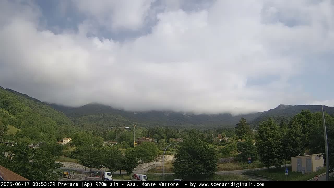 A cloudy day reveals a valley of green trees and buildings nestled beneath low-hanging clouds and mountains.