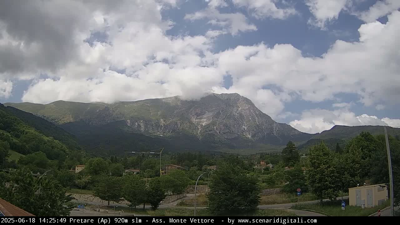 A partly cloudy sky overlooks a lush green valley and a large, imposing mountain.