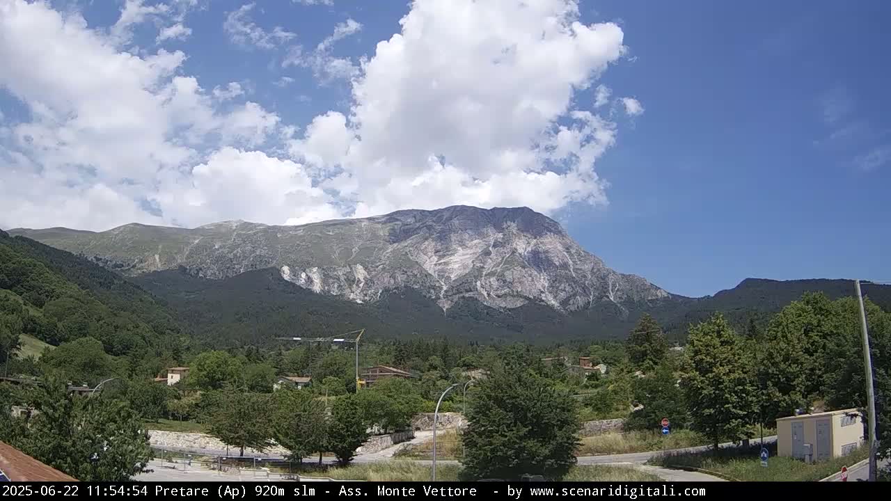 A large mountain with light-colored rock faces is visible in the background under a partly cloudy sky, with a small town situated in the foreground.