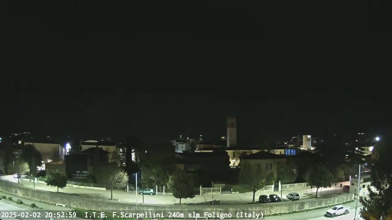 A nighttime view of a town with a few cars parked along a street, under a clear, dark sky.