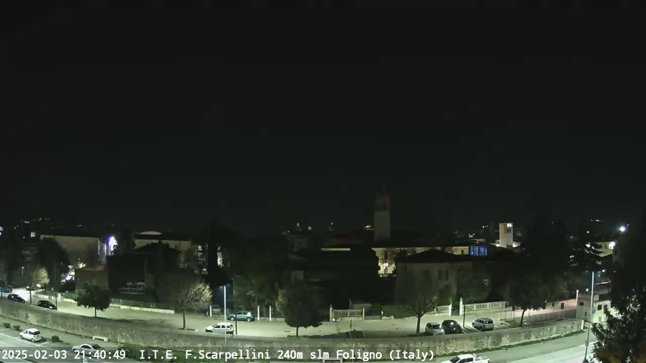 A nighttime view of a town with buildings and sparsely parked cars under a clear, dark sky.