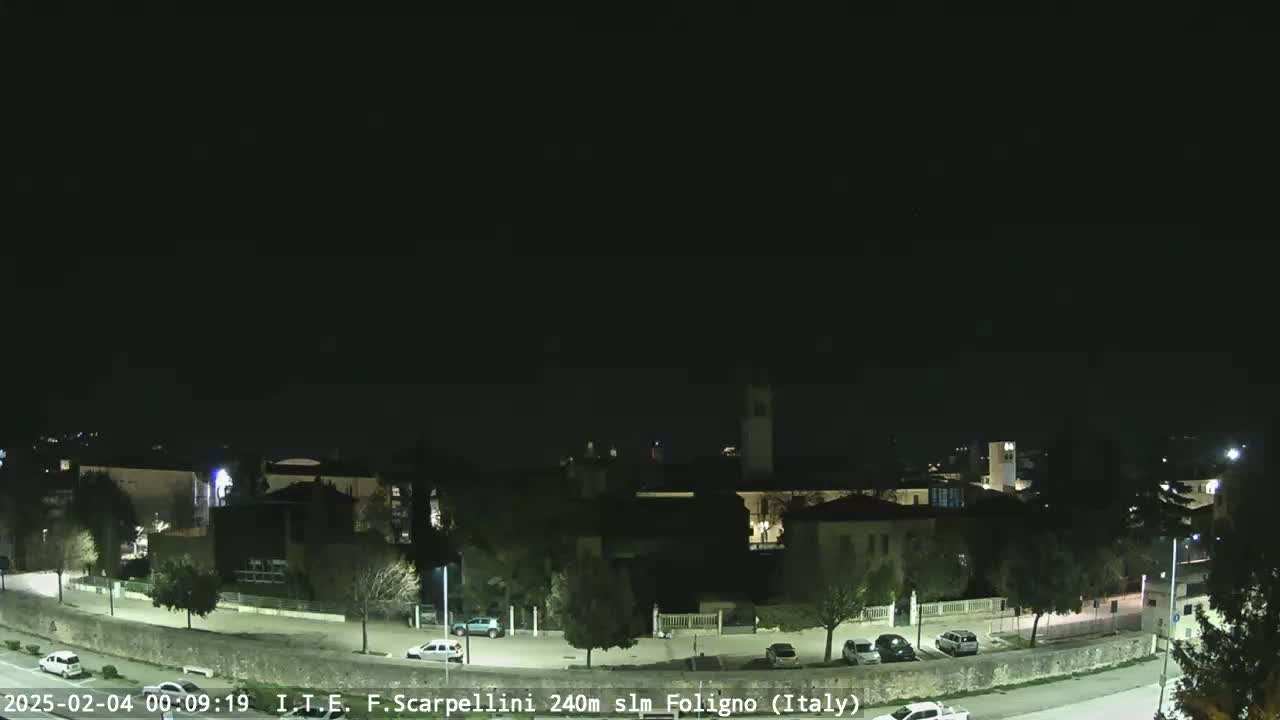 A nighttime, clear view of a town with buildings, roads, and parked cars.