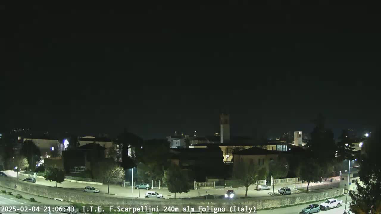 A nighttime view of a town with a few cars parked along a road, under a clear, dark sky.