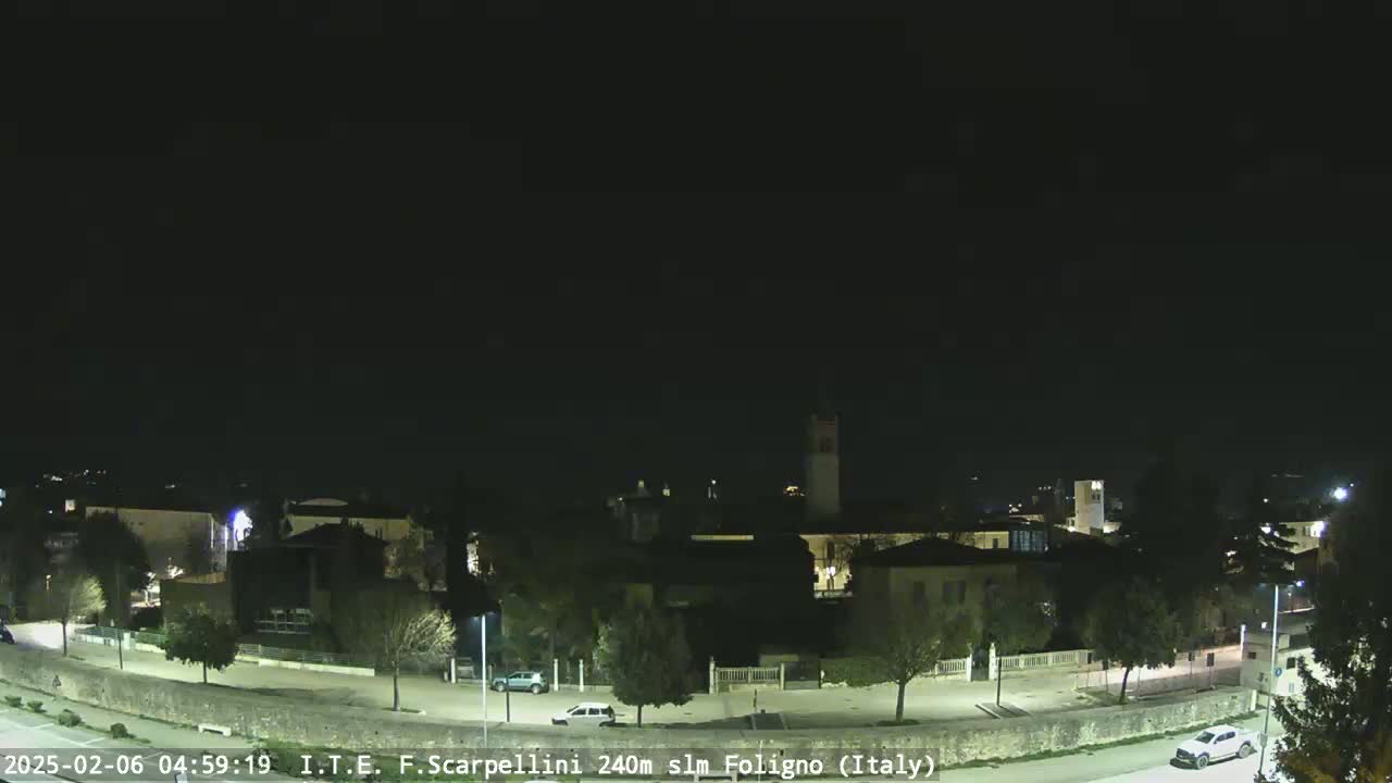 A nighttime view of a quiet town with a few cars on the roads, under a clear, dark sky.