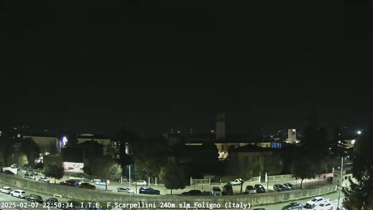 A nighttime view of a town with cars parked in a lot, under a clear, dark sky.