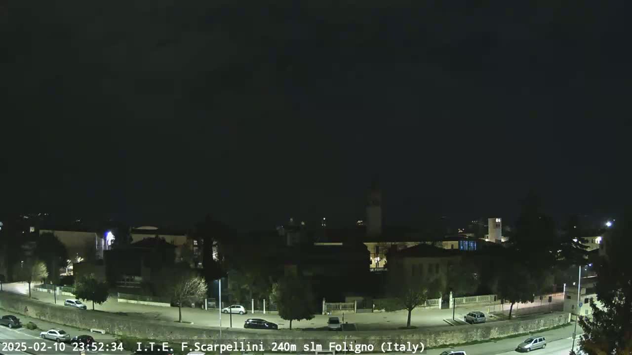 A nighttime view of a town with cars parked along a road, under a dark, clear sky.